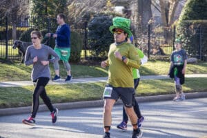 Tulsa USA 3 - 16 - 2019 Man in sequined green top hat surrounded by other people jogging down urban residential street in annual Saint Patrick's Day run