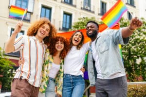 Multiracial friends hugging and waving rainbow flags while celebrating lgbt pride month